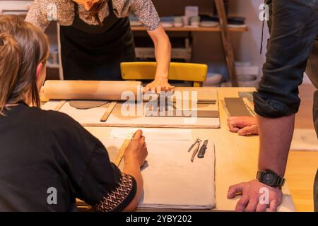 Participants in a ceramic workshop collaborate at a table, using tools and techniques to shape clay pieces. The environment is creative and focused, h Stock Photo