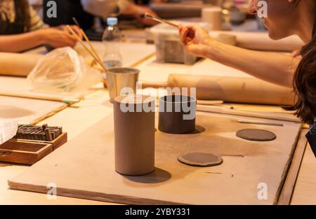 Bunch of people engaging in a creative ceramic workshop, focusing on pottery techniques. Hands are shaping clay with tools, depicting teamwork and art Stock Photo