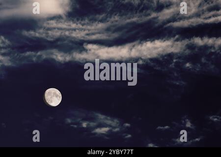 The moon illuminates a dark, cloudy sky, creating an atmospheric and moody night scene. Stock Photo