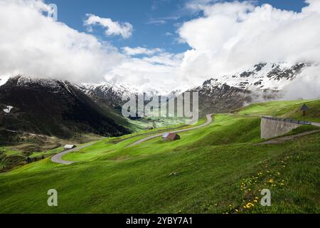 Alpine road winding down toward valley between snowed mountains. Stock Photo
