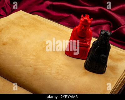 yellowed medieval ancient blank book open on a table with small statues representing figures of the King and Queen. Blank pages copy space area Stock Photo