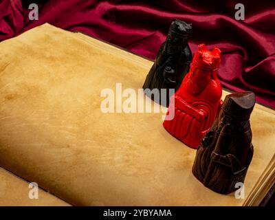 yellowed medieval ancient blank book open on a table with small statues representing figures of the King, the bishop and Queen. Blank pages copy space Stock Photo