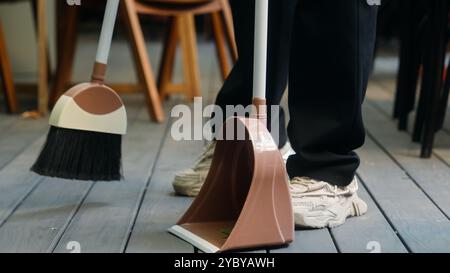 Indian Arabian man cafe worker in apron entrepreneur male businessman guy waiter cleaner working small business owner sweeping leaves using broom Stock Photo