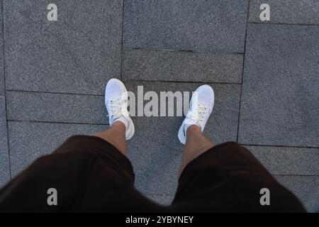 A guy in black shorts and white sneakers, standing on a granite tile. First-person view of the legs. High quality photo Stock Photo
