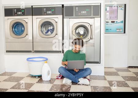Young man using laptop while doing laundry in a modern laundromat Stock Photo
