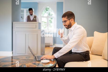 Businessman working on a laptop while enjoying coffee in a stylish lounge Stock Photo