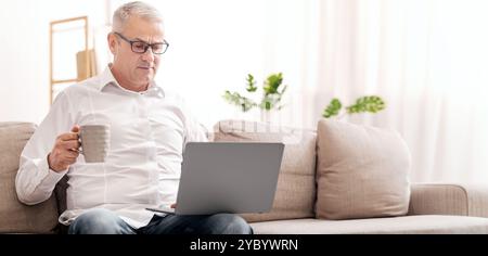 Elderly Man Using Laptop And Having Tea Stock Photo