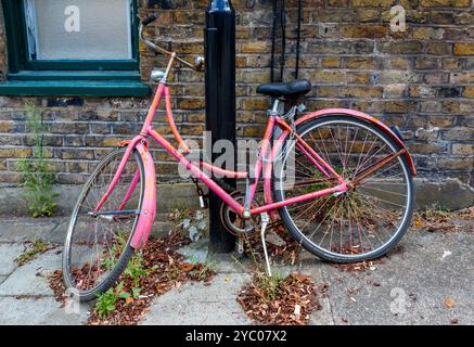 An abandoned women's pink roadster bicycle chained to a lamp post, London, UK Stock Photo