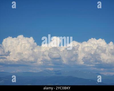 Aerial view of fluffy white cumulus clouds in a blue sky over distant mountains. Stock Photo