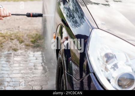 A Person Using a Pressure Washer to Clean a Car's Exterior in Bright Outdoor Light. Stock Photo