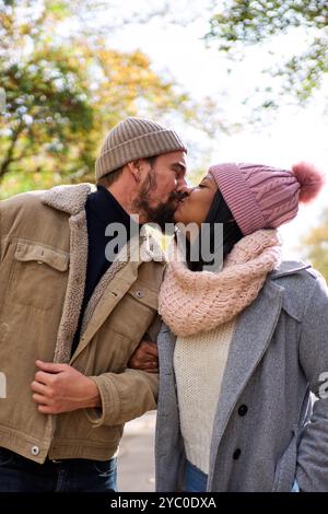 Lovely multiracial couple kissing while walking outdoors in winter time in the city. Stock Photo