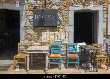 Rustic cafe with colourful wooden chairs and tables in front of a stone wall in the sunlight, Agios Nikolaos, Mani, Messenia, Peloponnese, Greece, Eu Stock Photo