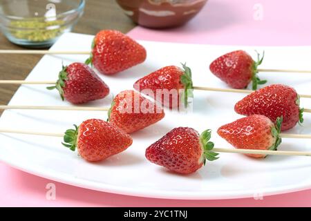 Strawberries on sticks on white plate. Process of cooking berries in chocolate.  Stock Photo