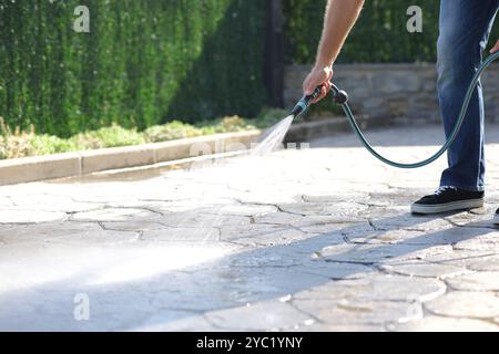 Close up of a man cleaning garden floor with water using hosepipe Stock Photo