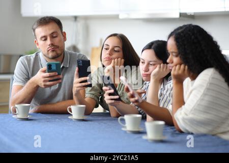 Bored friends ignoring them using their smart phones in the kitchen at home Stock Photo