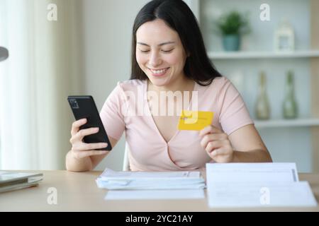 Happy asian woman paying bills with smart phone and credit card in a desk at home Stock Photo