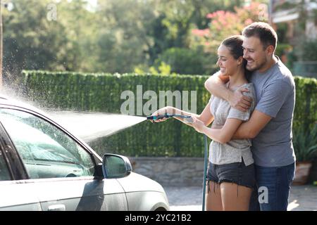 Happy couple washing car in the garden using hosepipe Stock Photo