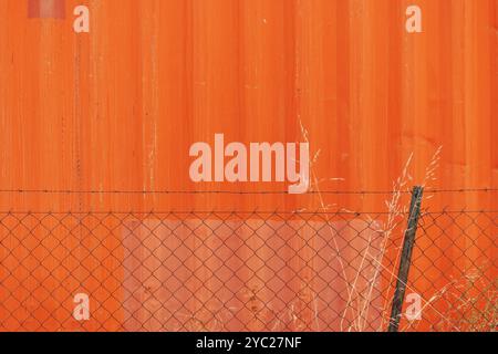 Orange background, industrial building and chain link fence with dry plants, copy space included Stock Photo