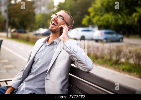 Portrait of cheerful businessman who is talking on phone. Man sitting on bench in the city and talking on phone. Stock Photo