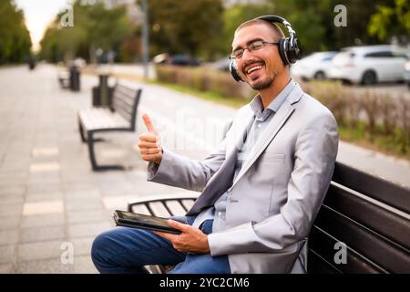 Portrait of happy businessman who is messaging on digital tablet. Man sitting on bench in the city and using digital tablet. Stock Photo