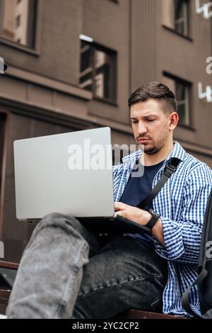 Young man working on a laptop while seated on a bench outside Stock Photo