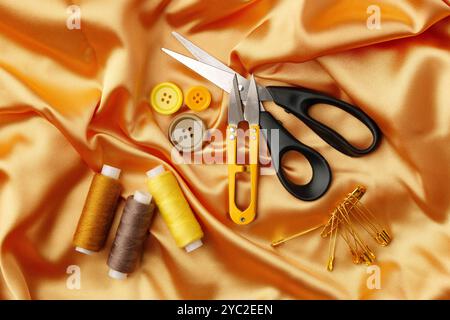 Crafting essentials arranged on golden satin fabric with sewing tools and colorful buttons scattered around Stock Photo