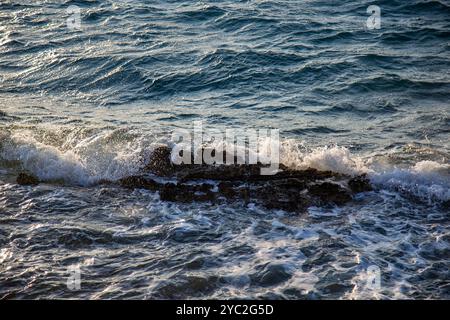 Waves crashing over a cluster of dark rocks, turbulent ocean Stock Photo