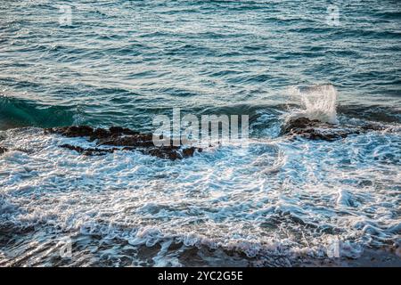 Waves crashing over a cluster of dark rocks, turbulent ocean Stock Photo