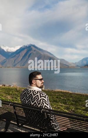 Side view of a stylish young adult man sitting on bench Stock Photo