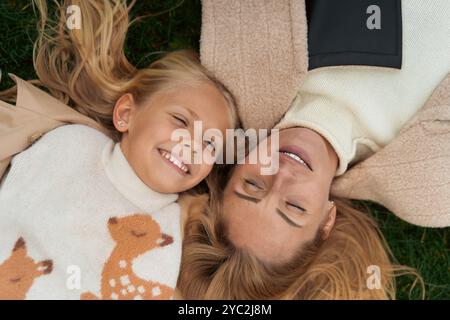 Mom and Daughter lie on the green grass and smile, happy autumn Stock Photo