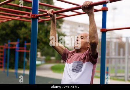 Sportive old man doing pull-ups outdoors Stock Photo