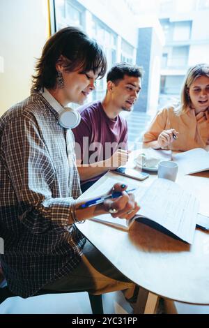 Young adults engaged in a university study session at a cafe, working collaboratively on a group project, showcasing teamwork and learning. Stock Photo