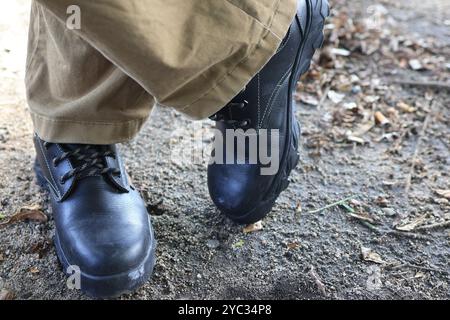 Close-up of sturdy black work boots on soil with foliage, showcasing their rugged design and durability. Stock Photo
