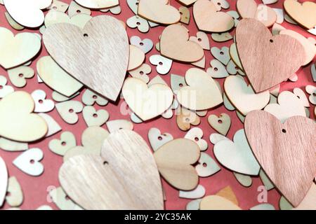 Four wooden hearts on top of a collection of slightly smaller wooden heart on top of a layer of even smaller hearts on a dark pink background Stock Photo