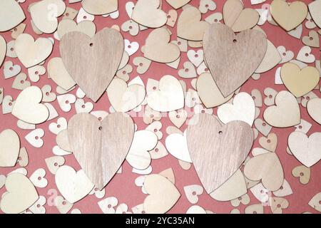 Four wooden hearts on top of a collection of slightly smaller wooden heart on top of a layer of even smaller hearts on a dark pink background Stock Photo