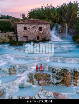 Visitors enjoy the soothing, thermal waters of Saturnia as the sun sets, casting a warm glow over the cascading pools. Saturnia thermal baths,Tuscany, Stock Photo