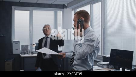 Work in modern office of international stock exchange company: Financial advisor, broker consulting investor client about investment, talking by phone. Nervous senior boss controls the negotiations. Stock Photo