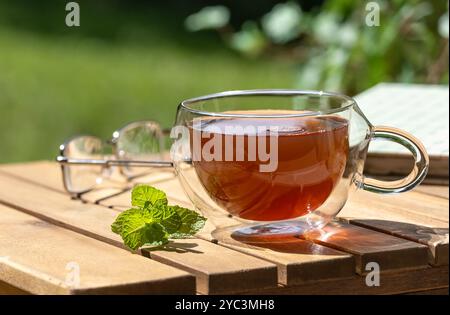 Cup of tea and mint on wooden table with eyeglasses and book with nature background for coppy space Stock Photo