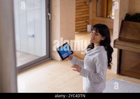 Smiling woman using tablet to control smart home system in cozy living room Stock Photo