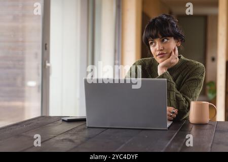 Woman working from home, using laptop and drinking coffee, feeling thoughtful Stock Photo
