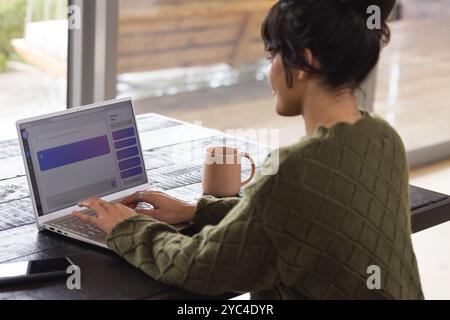 Woman chatting online using laptop at home, enjoying coffee break Stock Photo