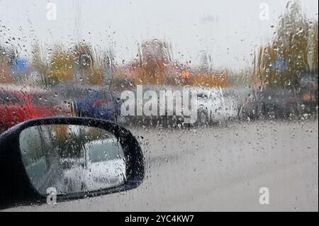 This photo captures a rainy day scene from inside a car, where raindrops have accumulated on the windshield, blurring the view of the outside. The sid Stock Photo