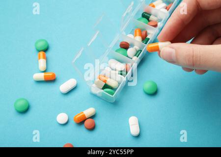 Female hand sorting pills in pillbox on blue background Stock Photo