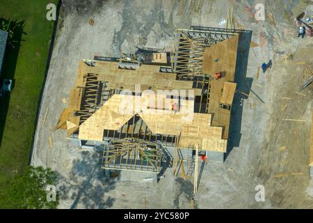 Aerial view of builders working on unfinished residential house with wooden roof frame structure under construction in Florida suburban area. Stock Photo