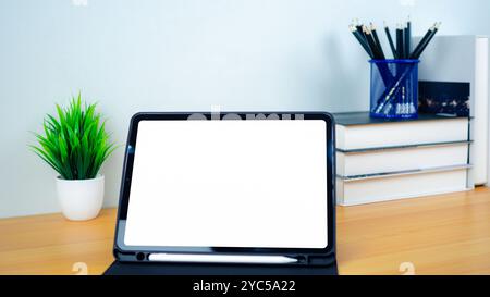Tablet with blank screen on wooden table. Office supplies, Books, Indoor plants, on wooden table and white wall. Space for copying your text, Workspac Stock Photo