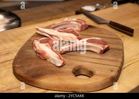 Four raw lamb chops on a wooden kitchen work top ready to be cooked Stock Photo