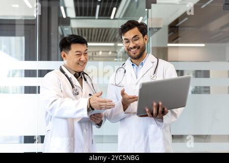 Two doctors engaged in collaboration, discussing medical data on a laptop in a modern office. Emphasis on teamwork, technology, healthcare, and profes Stock Photo