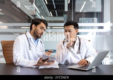 Doctors engaged in discussion over patient diagnosis in an office setting, utilizing tablet and laptop. Emphasizing teamwork, collaboration, healthcar Stock Photo