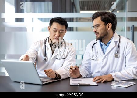 Doctors in formal attire collaborate using laptop in office, discussing patient details. Focus on teamwork, medical professionalism, digital communica Stock Photo