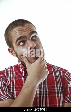 Young man wearing a red checkered shirt is deep in thought, his hand resting on his chin as he gazes upward in contemplation Stock Photo